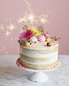 a white cake topped with lots of pink and yellow flowers next to a sparkler