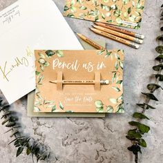 the wedding stationery is laid out next to some pens and pencils, along with two envelopes