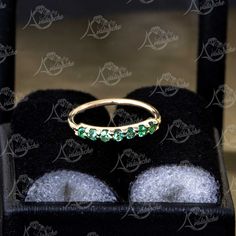 a gold ring with green stones sits on top of a black velvet display case,