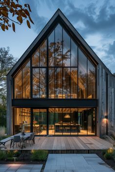 a modern house with large windows and wooden decking at dusk, lit up by outdoor lighting