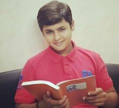 a young boy sitting on a couch reading a book