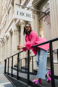 a woman leaning on the railing of a building with her pink coat over her shoulders