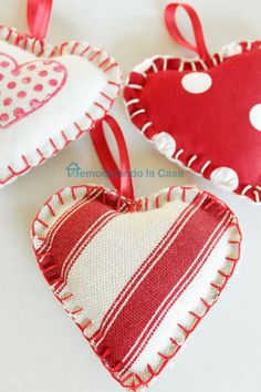 three red and white heart shaped ornaments hanging on a table with ribbon around the edges