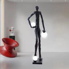 a black statue with two white balls in it's hands and a red chair behind it