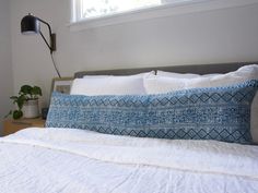 a bed with white linens and blue pillows on top of it next to a window