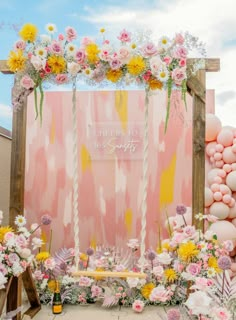 a pink and yellow wedding backdrop with flowers, balloons and other decorations on the ground