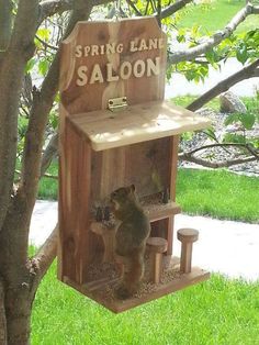 a wooden birdhouse with a bear inside it sitting in the grass next to a tree