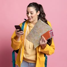 a woman holding a map and looking at her cell phone while standing in front of a pink background