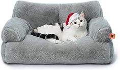 a black and white cat wearing a santa hat sitting in a gray chair with its paws on the pillow