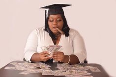 a woman sitting at a table with money in front of her and wearing a graduation cap