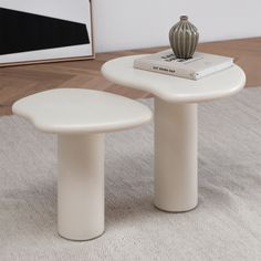 two white tables sitting on top of a carpeted floor next to a book and vase