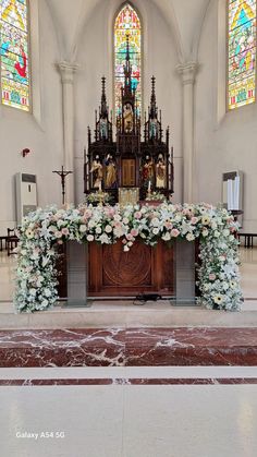 an altar decorated with flowers in front of two stained glass windows at the end of a church