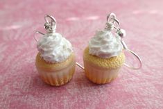 two small cupcakes with white frosting and silver earwires on a pink background