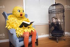 a woman sitting in a blue chair next to a bird cage and holding a book