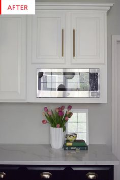 a kitchen with white cabinets and flowers in a vase next to the microwave on the wall