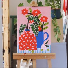 an easel with a painting on it in front of some potted plants and flowers