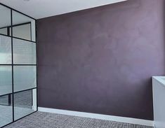 an empty room with a purple wall and glass partitions to the side, in front of a white sink