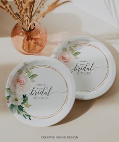 two paper plates with flowers on them sitting next to a vase filled with dry grass