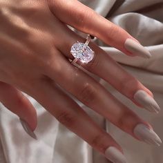 a woman's hand with white manicured nails and an oval shaped diamond ring