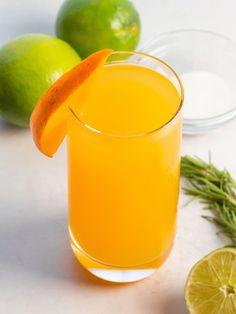 a glass filled with orange juice next to limes