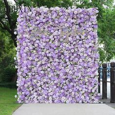 a large purple flower covered wall next to a sidewalk