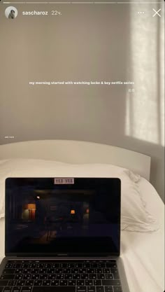 an open laptop computer sitting on top of a white bed covered in pillows and blankets