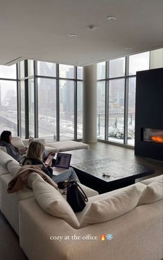 two women sitting on a couch in front of a fire place using their laptops