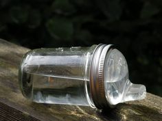 an empty glass jar sitting on top of a wooden table next to a tree trunk