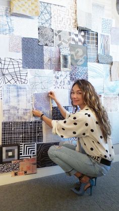 a woman kneeling down in front of a wall covered with different types of tiles and patterns