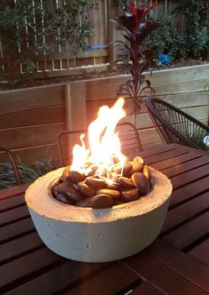 a fire pit sitting on top of a wooden table next to a planter filled with rocks