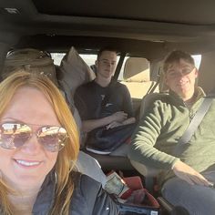 three people sitting in the back seat of a car, one with sunglasses on his head