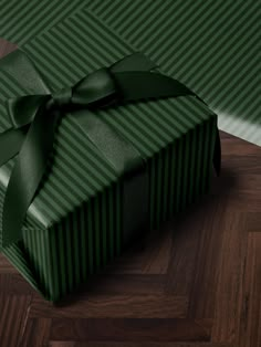 a green gift box with a large bow on it's side sitting on a wooden floor