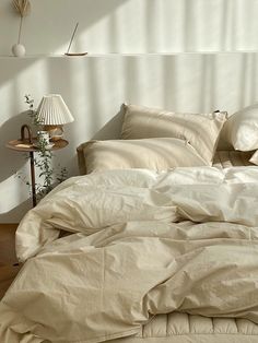 an unmade bed with white sheets and pillows on top of it next to a lamp