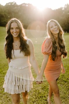 two young women holding hands and walking in the grass with sun shining on their faces