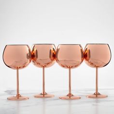 four wine glasses lined up in a row on a marble counter top with one empty