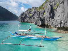 two blue boats tied to the side of a rocky cliff in clear water with mountains in the background