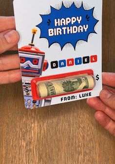 someone holding up a birthday card with a roll of money in front of it and a robot on the back