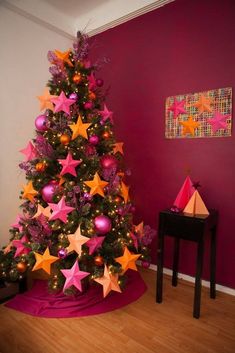 a decorated christmas tree with pink and orange stars in the center, against a red wall