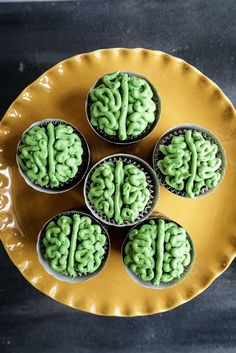 four cupcakes with green frosting in the shape of a brain on a yellow plate