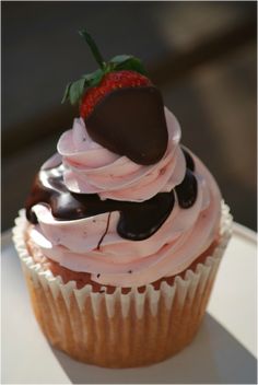 a chocolate cupcake with pink frosting and a strawberry on top is sitting on a white plate