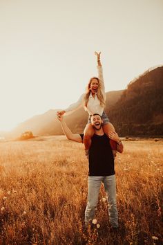 a man carrying a woman on his shoulders in the middle of an open field at sunset