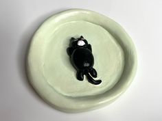 a black cat figurine sitting on top of a white plate with its eyes closed