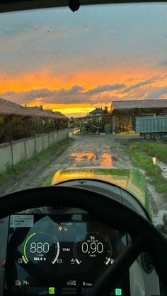 the view from inside a vehicle driving down a dirt road at sunset, with rain drops on the windshield