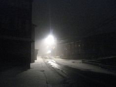 a street light shining in the dark with snow on the ground and buildings around it