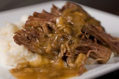 a white plate topped with meat and gravy on top of mashed potatoes