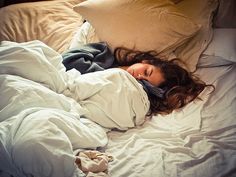 a woman laying in bed with her head on the pillow and she is covered by an overstuffed blanket