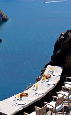 a long table with plates and glasses on it next to the water in front of an island