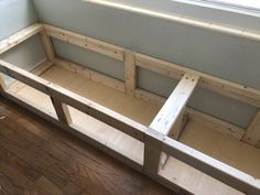 a bench made out of wood sitting on top of a hard wood floor next to a window