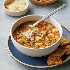 a white bowl filled with soup next to bread and crackers on a blue plate