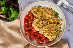 two pieces of chicken on a plate with tomatoes and lettuce next to it